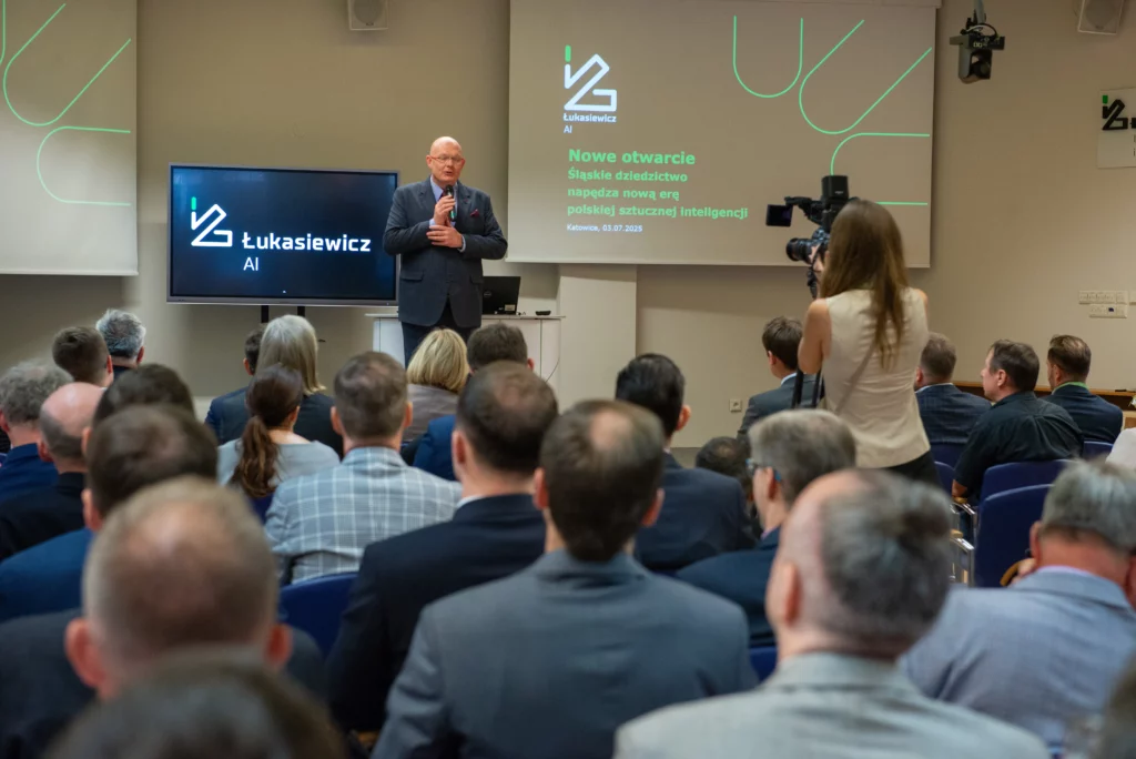 Mężczyzna przemawia stojąc na scenie na auli pełnej słuchaczy